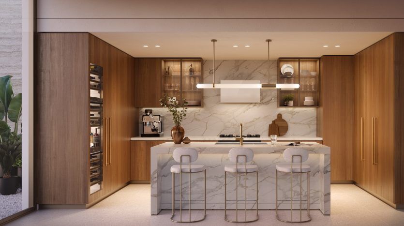 Une cuisine moderne avec des armoires en bois et un îlot en marbre doté de trois tabourets de bar, d'appareils intégrés et de suspensions complètent le design élégant de cet appartement de Dubaï.
