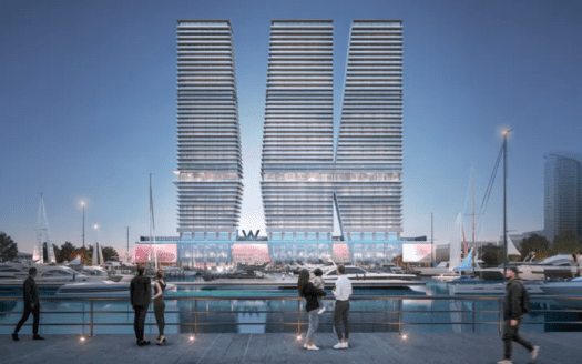 Une scène moderne au bord de l’eau au crépuscule présente deux grands bâtiments identiques avec des lignes horizontales formant une forme en V. Les gens socialisent le long de la promenade, avec au premier plan les yachts amarrés dans la marina. La zone est éclairée par un éclairage d’ambiance.