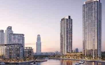 Des tours modernes et des appartements en bord de mer entourent le port de plaisance de Creek Bay, avec des yachts, des palmiers et une voie d'eau calme, sous un ciel doux en début de soirée.
