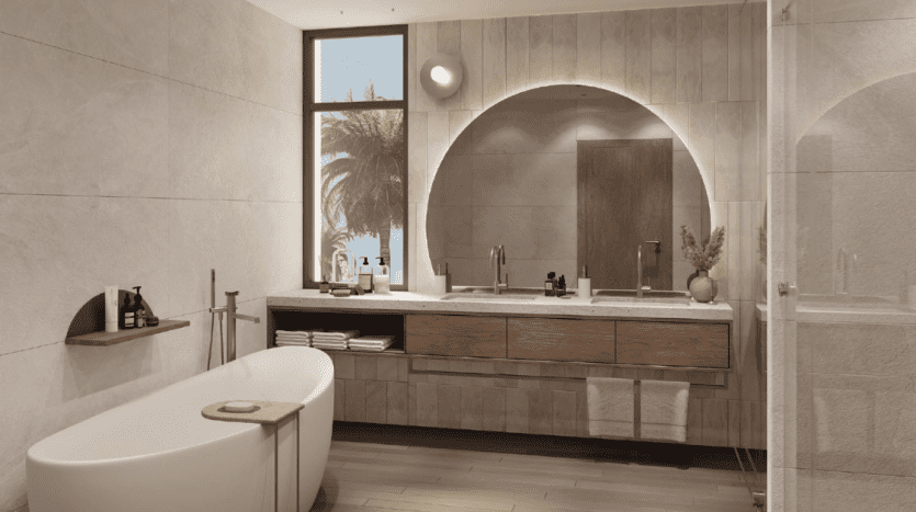 Salle de bain moderne avec un grand miroir au dessus d'une vasque en bois, une baignoire autoportante et une cabine de douche. Une fenêtre révèle des palmiers à l'extérieur, mélangeant les éléments intérieurs et extérieurs dans cet immobilier recherché