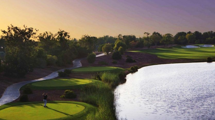 Un golfeur jouant sur un parcours de golf serein au coucher du soleil, entouré d'une verdure luxuriante, d'un sentier lisse et d'un grand lac réfléchissant à proximité d'une villa exclusive à Dubaï.