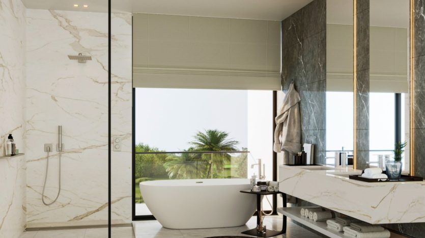 Une salle de bains luxueuse dans une villa à Dubaï, avec des murs en marbre, une grande baignoire près d'une baie vitrée donnant sur un paysage luxuriant, des lavabos à double vasque et une douche vitrée.