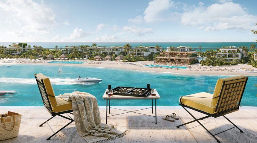 Deux chaises longues et une table sur laquelle est posé un jeu de backgammon — l’endroit idéal pour déguster une bonne bouteille de Château Piétrus — donnent sur un lagon turquoise, une plage de sable, des palmiers et les bâtiments du complexe hôtelier. Un yacht navigue sur l’eau sous un ciel bleu parsemé de nuages.