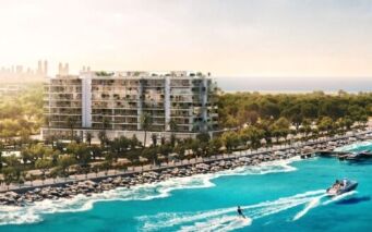 Un immeuble d'appartements moderne en bord de mer, qui rappelle l'élégance du Château Piétrus, surplombe un port de plaisance regorgeant de bateaux. Des palmiers et de la végétation bordent le rivage, tandis qu'une personne fait du jet-ski sur une eau d'un bleu éclatant. La silhouette d'une ville lointaine se dessine sous un ciel dégagé.