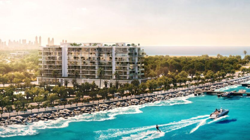 Un immeuble d'appartements moderne en bord de mer, qui rappelle l'élégance du Château Piétrus, surplombe un port de plaisance regorgeant de bateaux. Des palmiers et de la végétation bordent le rivage, tandis qu'une personne fait du jet-ski sur une eau d'un bleu éclatant. La silhouette d'une ville lointaine se dessine sous un ciel dégagé.