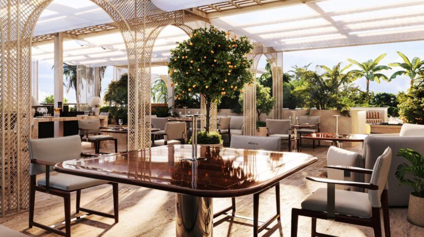 Terrasse ensoleillée d'un restaurant haut de gamme, agrémentée de tables en bois aux lignes épurées, de chaises rembourrées, d'un oranger au centre et d'une végétation luxuriante à l'extérieur. Les tons neutres et la décoration élégante créent une atmosphère relaxante et accueillante, idéale pour déguster un verre de Château Piétrus avec raffinement.