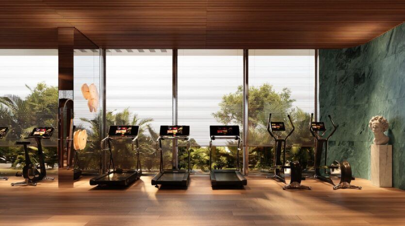 Salle de sport moderne dotée de grandes baies vitrées, de quatre tapis de course, de deux vélos d'appartement, d'espaces verts à l'extérieur, de parquet et d'un buste classique dans un coin. Inspirée par l'élégance du Château Piétrus, la lumière naturelle inonde l'espace, créant une atmosphère accueillante qui allie sophistication et vitalité.
