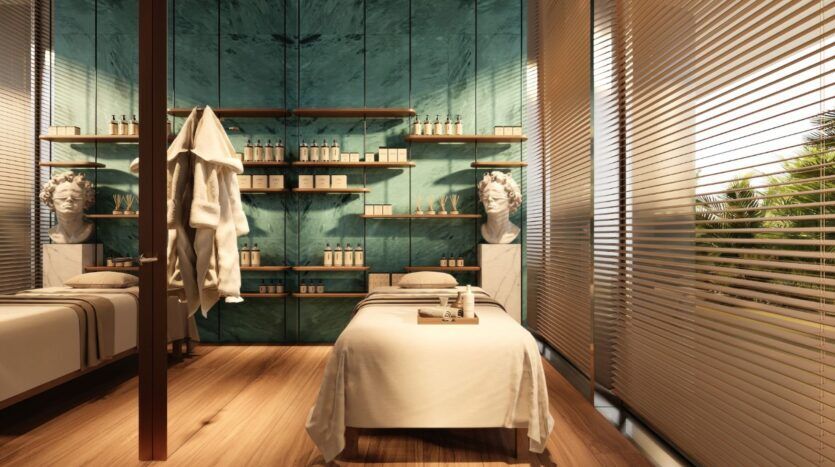 Une salle de spa moderne, dotée d'une table de massage, d'un parquet, d'étagères remplies de produits, de murs en marbre, de bustes classiques et baignée par la lumière du soleil qui filtre à travers les stores pour créer une ambiance sereine, évoque l'élégance raffinée du Château Piétrus.