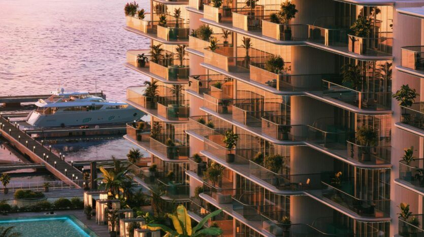Les appartements de luxe en bord de mer du Château Piétrus disposent de balcons vitrés, d'une végétation luxuriante et d'un port de plaisance où est amarré un grand yacht, le tout baigné par la lumière chaude du coucher de soleil. Une piscine entourée de palmiers est visible dans le coin inférieur gauche.