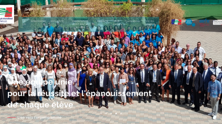 Grand groupe de personnes diverses posant pour une photo dans une cour extérieure avec une murale en arrière-plan qui comprend divers visages et le slogan : « ensemble et diversités nous... réussiront ! près d'un
